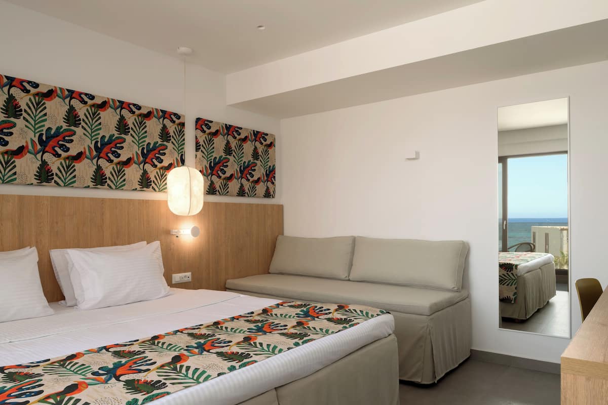 A hotel room with a bed, a sofa, a large mirror, and a view of the sea.