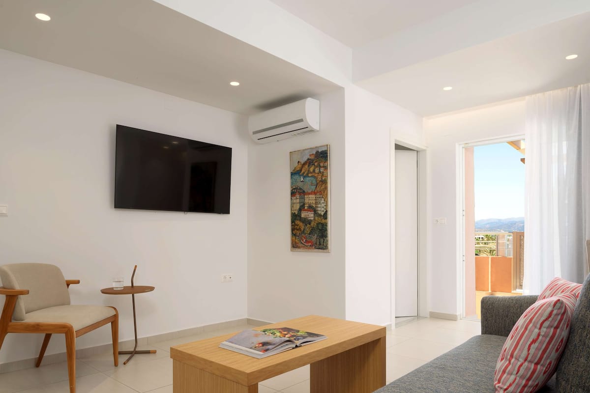 A modern living room with a flat-screen TV, a small round table, a sofa, and a balcony with curtains.