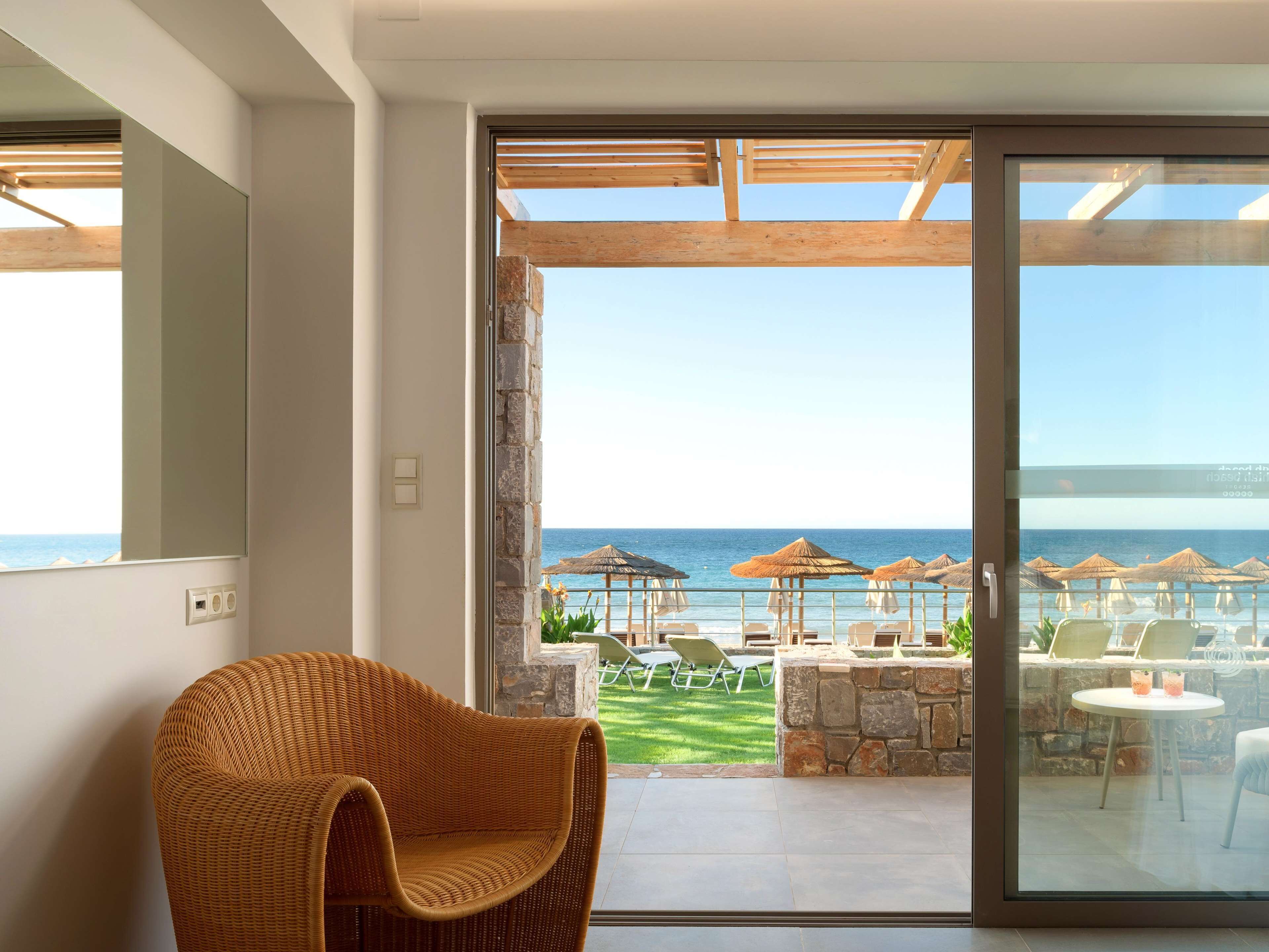 Una habitación moderna con un amplio ventanal corredero que da a un balcón con vistas al mar y sombrillas de playa.