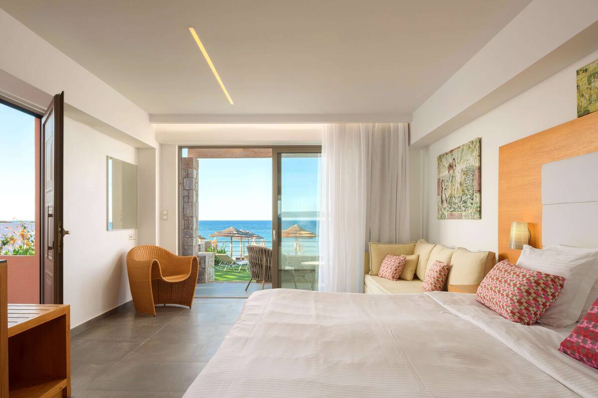 A modern hotel room with a large bed, a sofa, and a view of the ocean.
