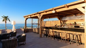 Un bar situé en bord de mer, avec des meubles en bois et une vue sur l’océan.