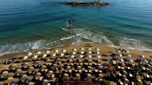 Une plage dotée de nombreux parasols et de chaises longues, un promontoire rocheux qui s’avance dans l’eau et une vue dégagée sur la mer.