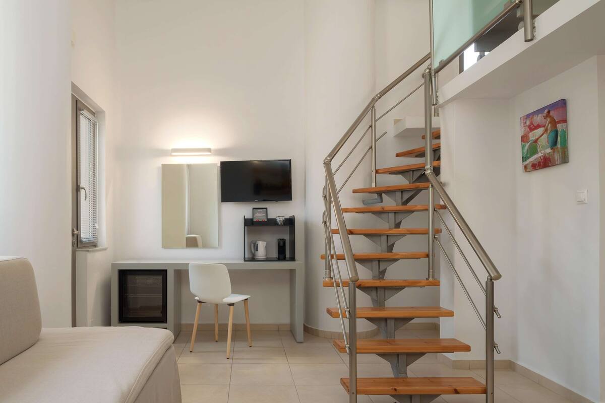 A modern living room with a sofa, a desk, a TV, and a staircase.