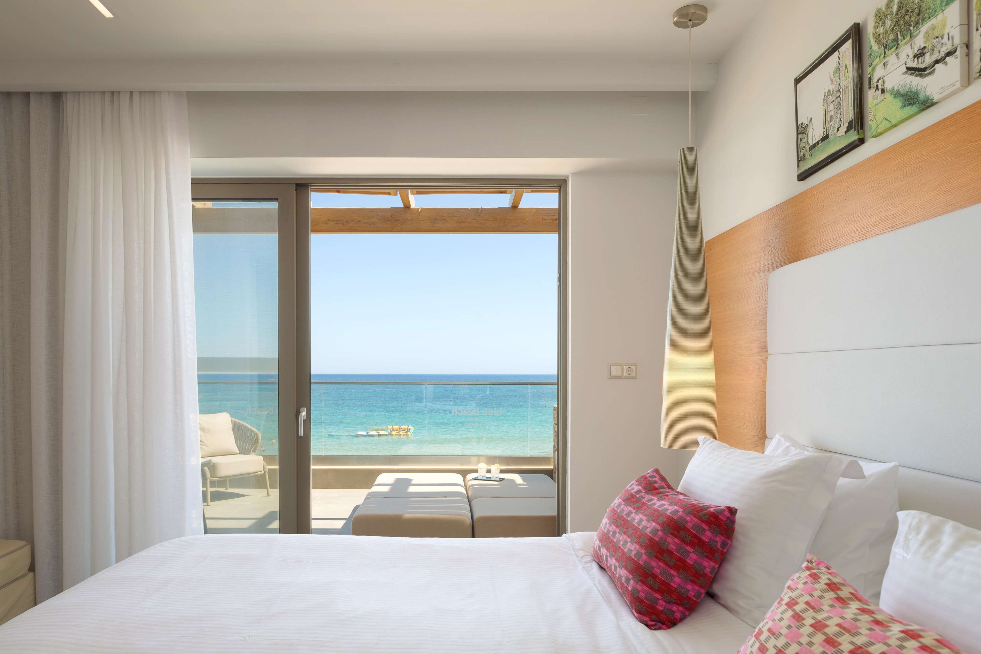 Ein Hotelzimmer mit Bett, einem Balkon mit Meerblick und einem Fenster mit Vorhängen.