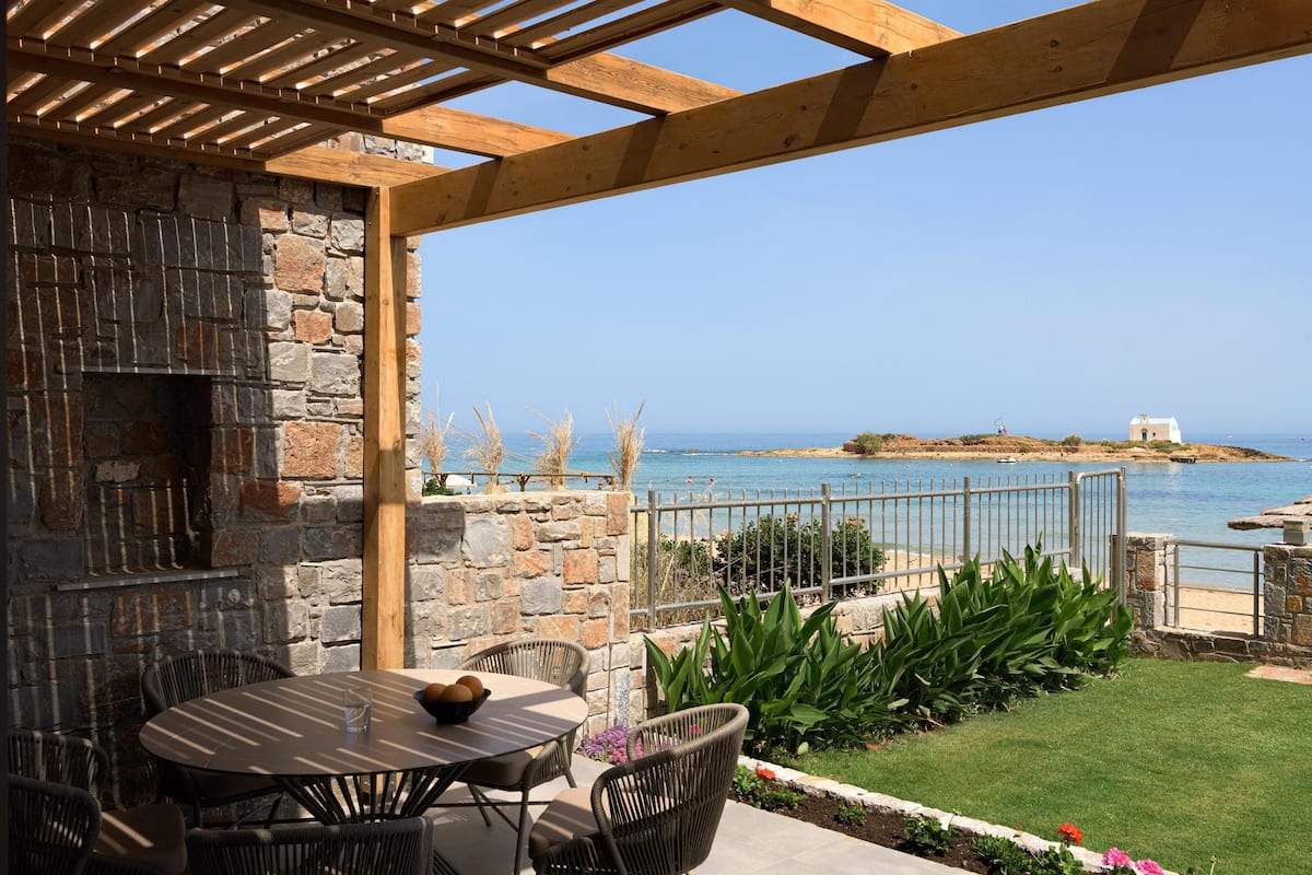 An outdoor patio with a stone wall, a wooden pergola, and a view of the sea.