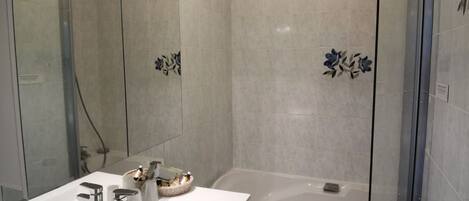 Un baño moderno con un espejo grande, dos lavamanos, una bañera y una cabina de ducha con paredes de vidrio.