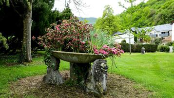 Un jardin avec un bac en pierre contenant des fleurs roses, entouré de pelouse et d’arbres.