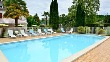 A swimming pool with lounge chairs and umbrellas, surrounded by a fence and various trees.