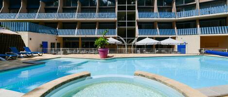 A hotel with a swimming pool, multiple balconies, and lounge chairs.