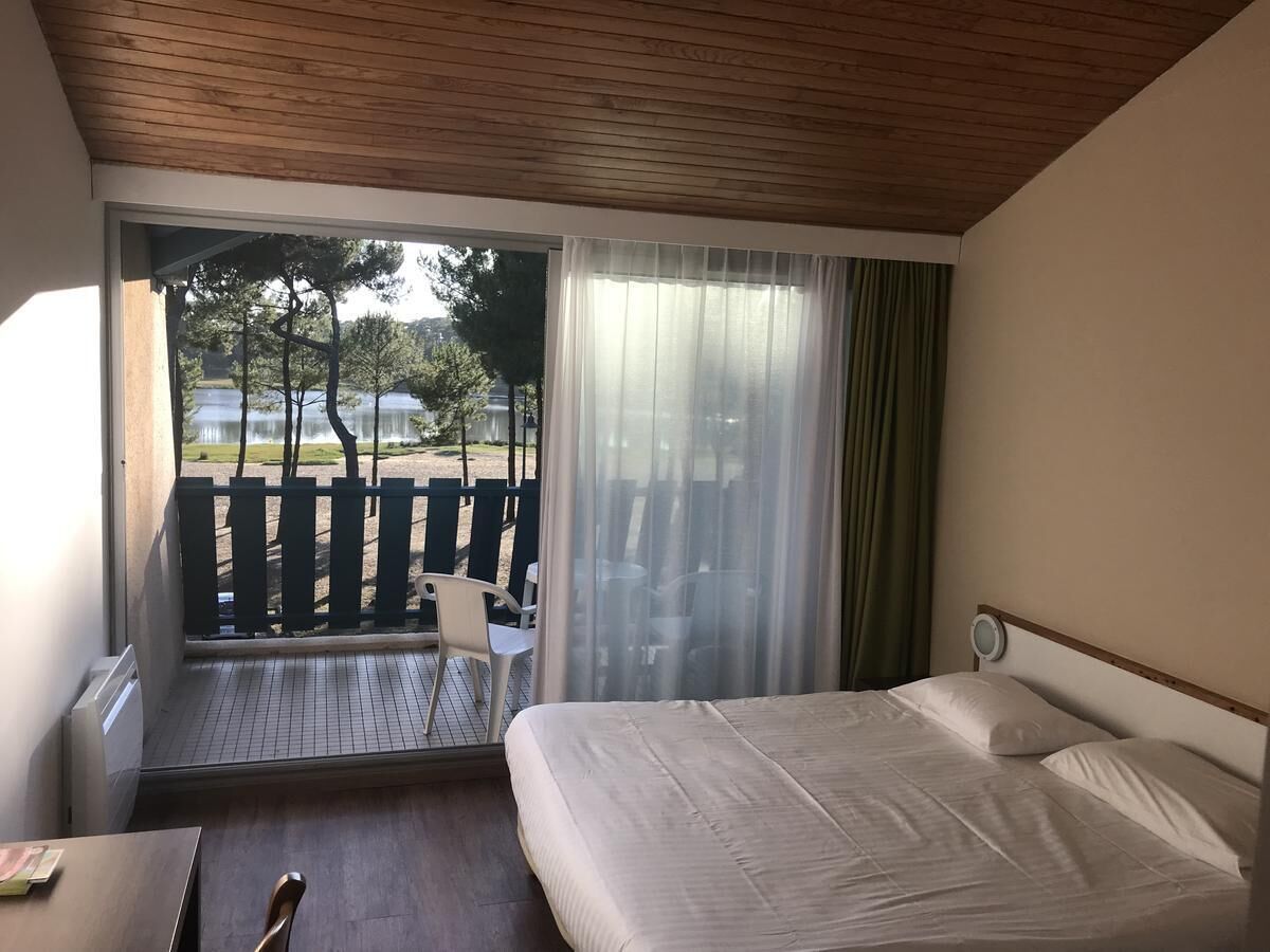 A hotel room with a bed, a desk, a chair, a window with curtains, and a view of the outdoors.