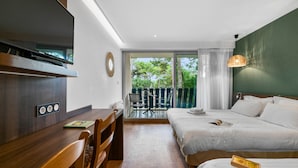 A hotel room with a bed, a desk with a chair, a television, and a balcony with chairs. - Lacotel (Soorts-Hossegor)