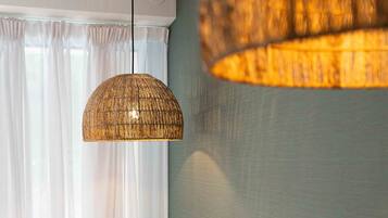 A hotel room with a bed, a hanging woven light fixture, and sheer curtains.