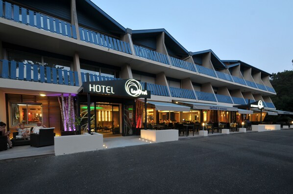 A hotel with a modern design, featuring a prominent 'HOTEL' sign, outdoor seating, and a well-lit entrance. - Lacotel (Soorts-Hossegor)