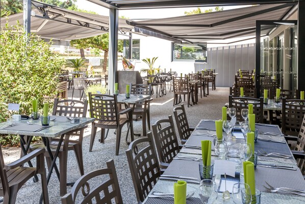Un área de comedor al aire libre con mesas preparadas para dos, cada una con un número, sillas y servilletas verdes.