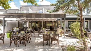 Une terrasse extérieure avec plusieurs tables et chaises, un espace salon couvert et un bâtiment en arrière-plan.
