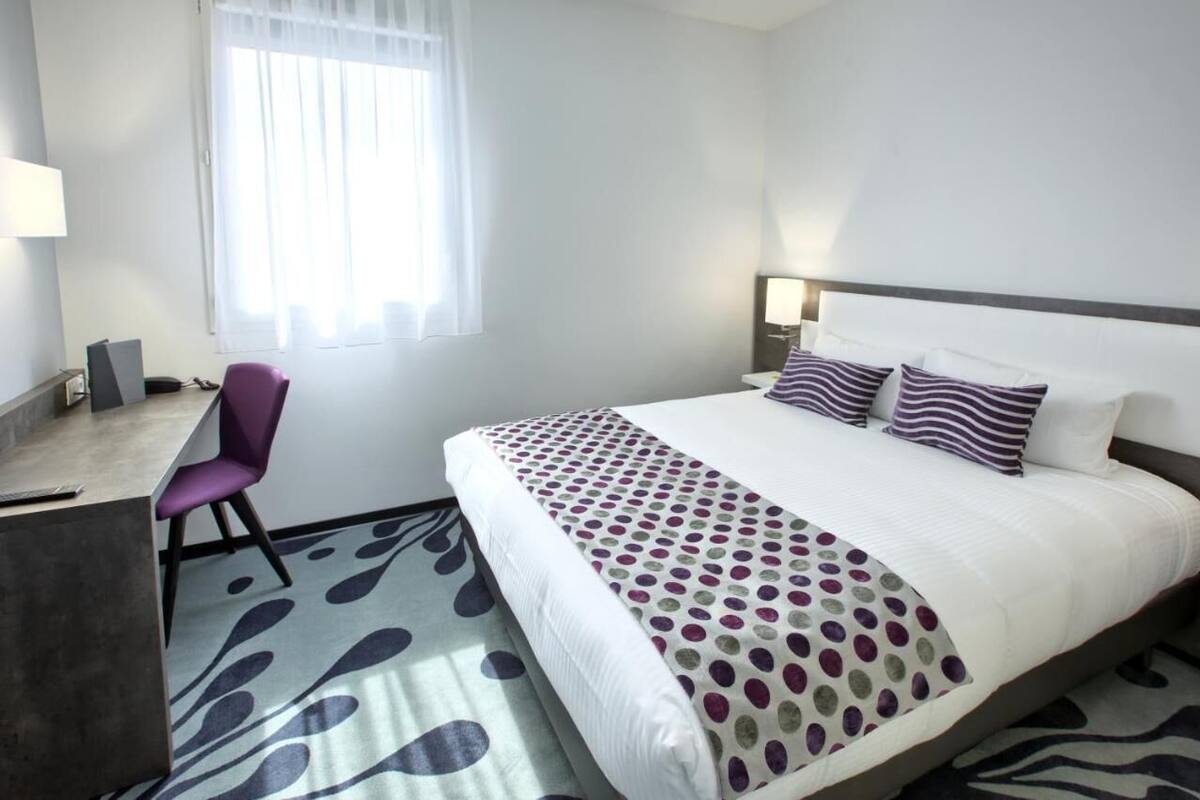 Een hotelkamer met een bed, bureau, stoel en raam met gordijnen.