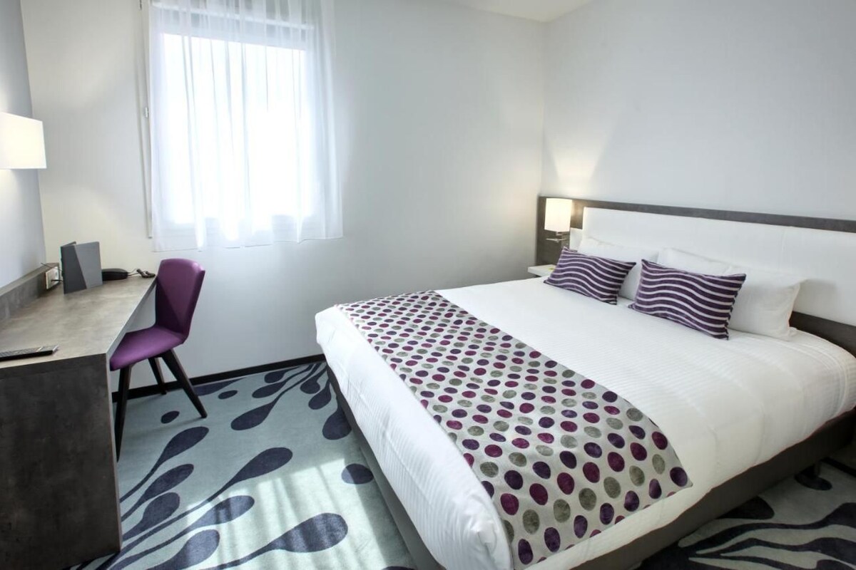 Een hotelkamer met een bed, bureau, stoel en raam met gordijnen.