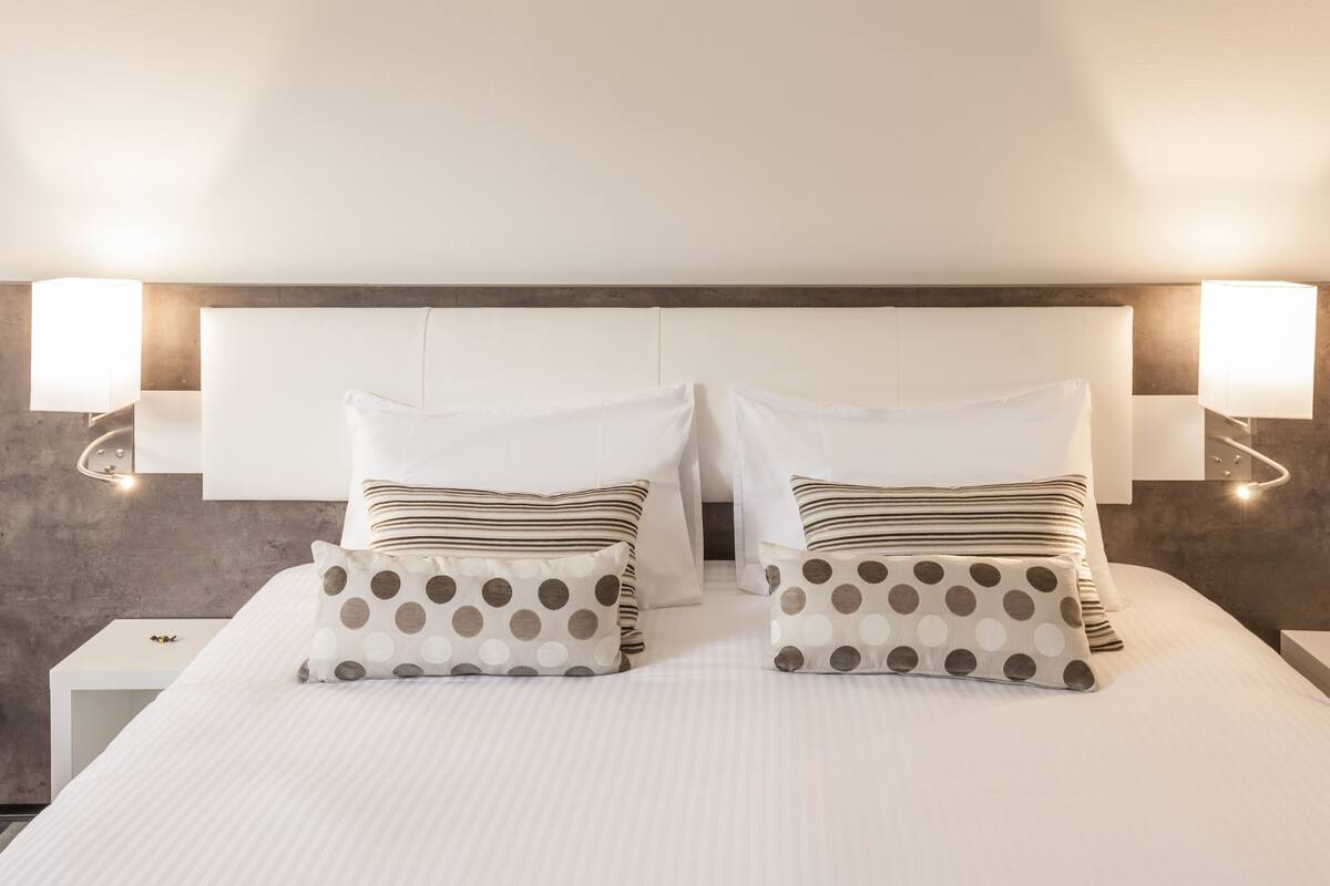 Een net opgemaakt bed met witte beddengoed en twee kussens, waarvan één met stippen en de ander gestreept.