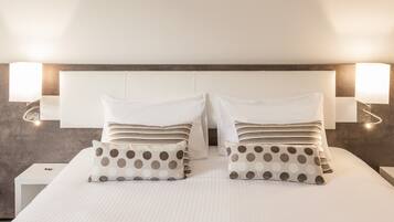A neatly made bed with white bedding and two pillows, one with a polka dot pattern and the other striped.