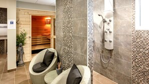 Une salle de bain moderne avec une douche, deux fauteuils en osier et un mur recouvert de mosaïques.