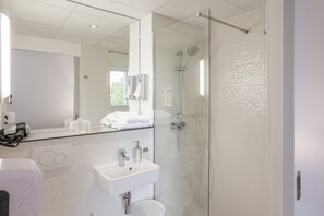 Een moderne badkamer met een douchecabine van glas, een witte wastafel en een grote spiegel.