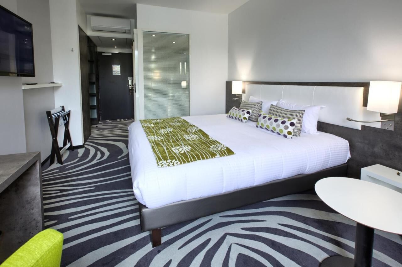 Ein Hotelzimmer mit Bett, Nachttischen, Schreibtisch, Sessel und Fernseher.