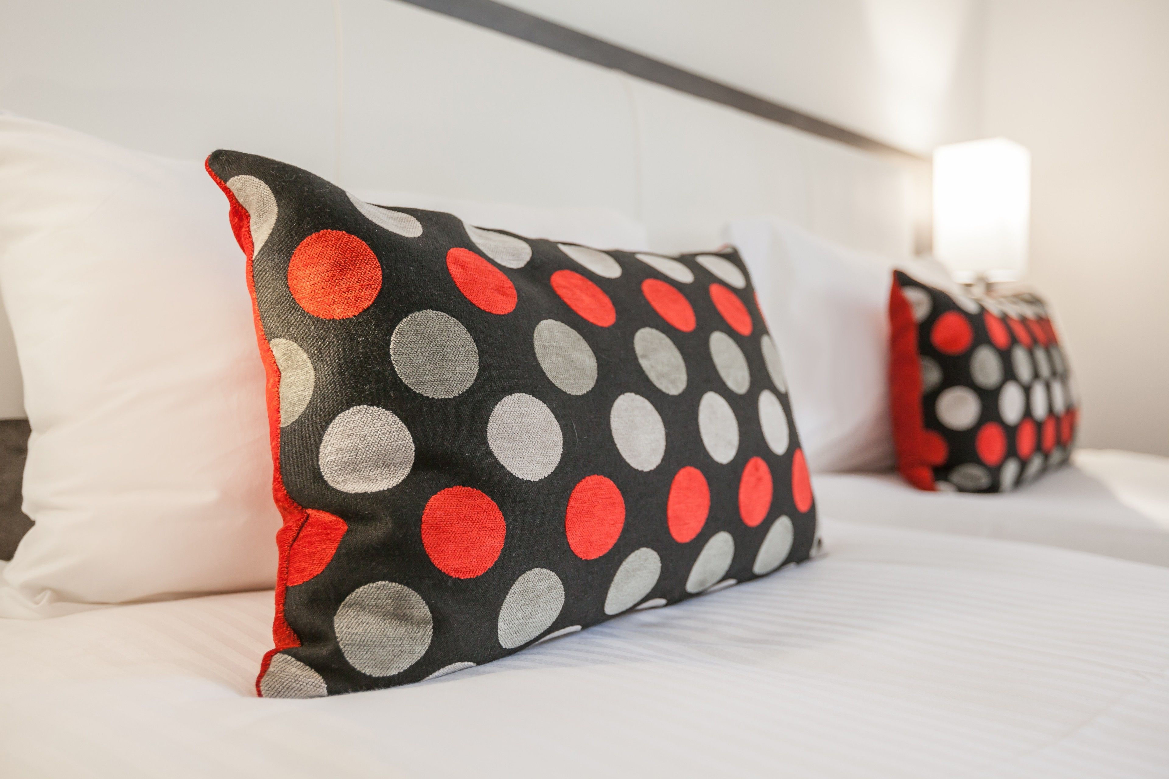 A bed with white bedding and two pillows with a polka dot pattern.