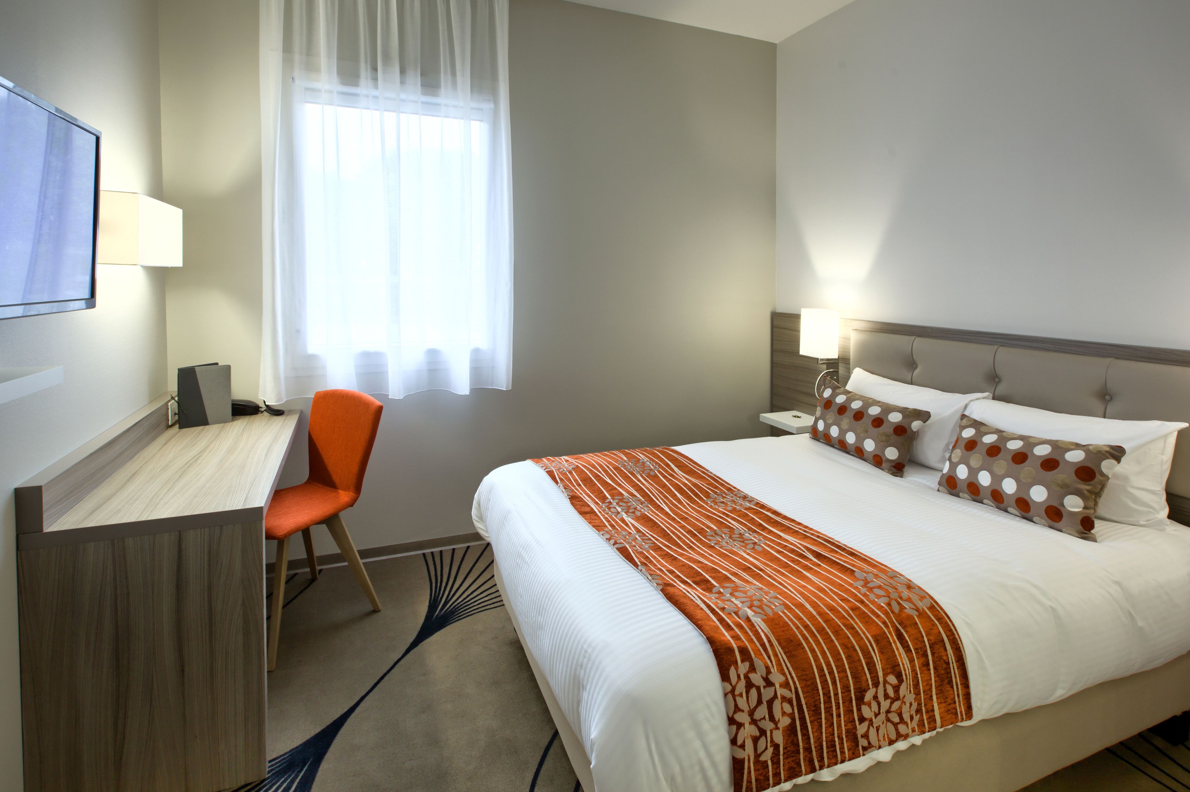 A hotel room with a bed, a desk, and a chair.