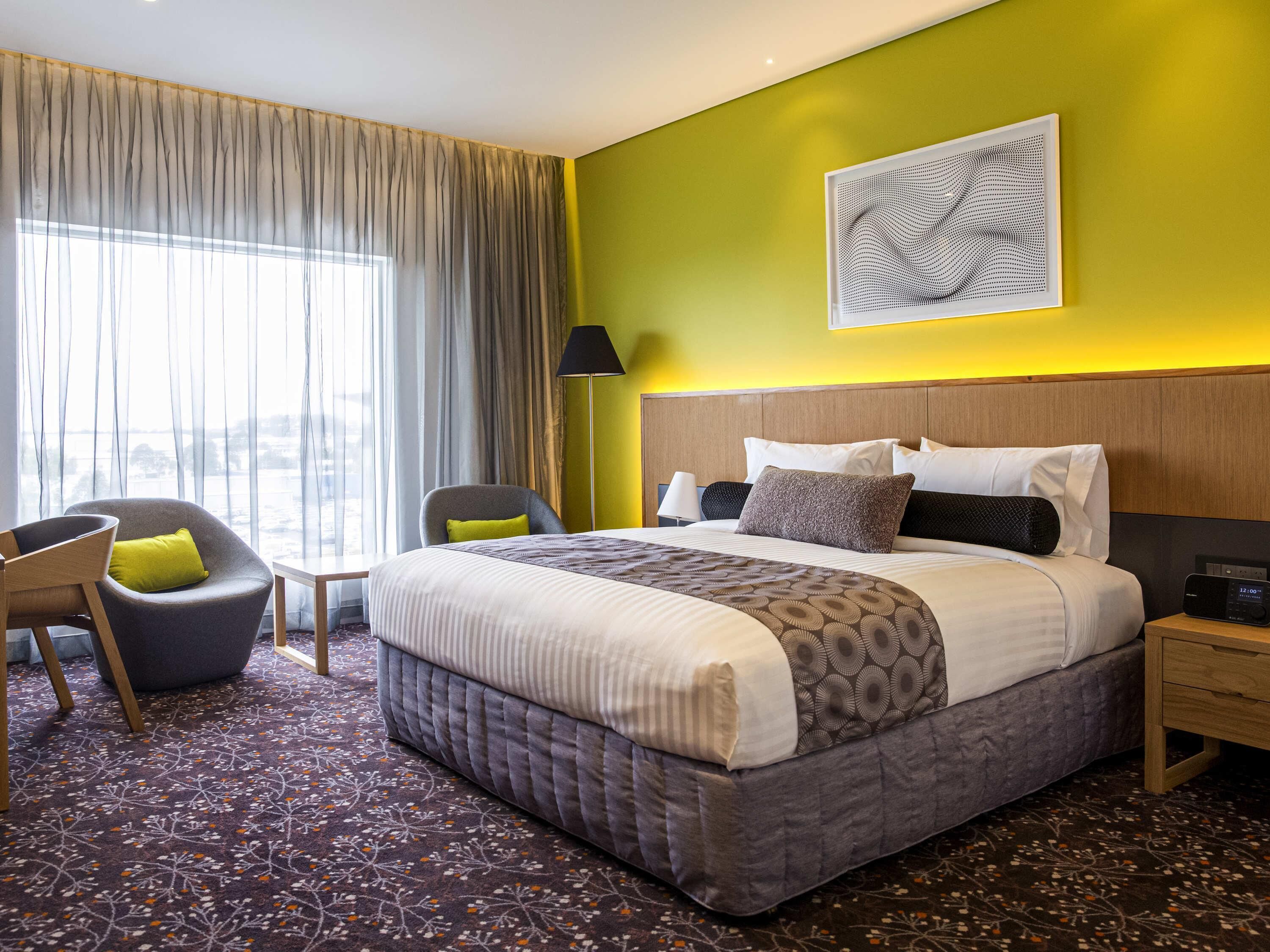 Habitación de hotel con cama, una silla, una lámpara y vistas al exterior.
