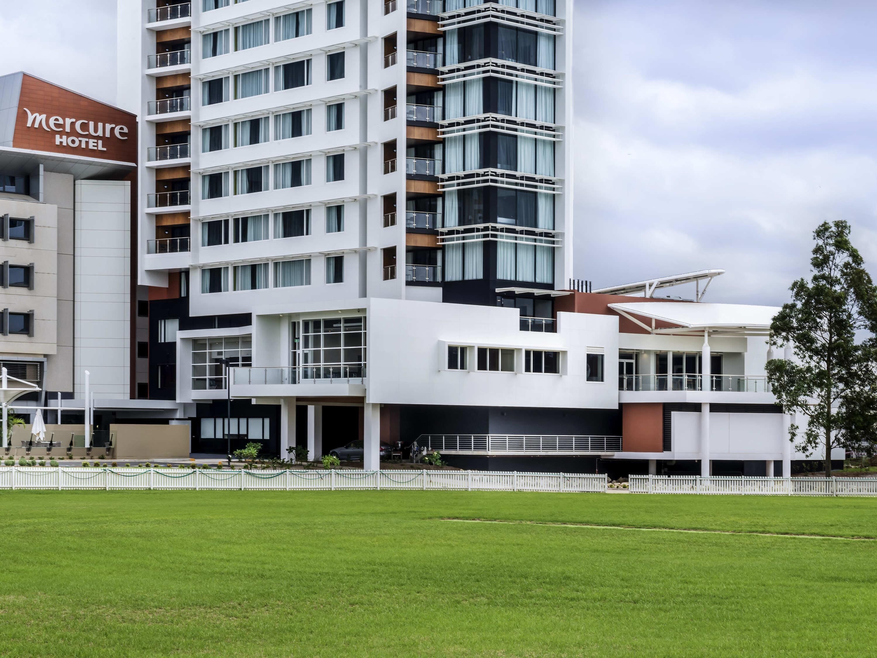 Moderni hotelli, jossa on useita kerroksia, selkeästi näkyvä «Mercure Hotel» -kyltti ja hyvin hoidettu nurmikko edessä.