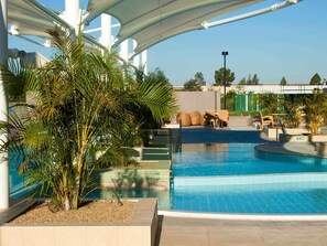 A swimming pool with a sunshade structure, surrounded by palm trees and outdoor seating. - Mercure Sydney Liverpool (Prestons)
