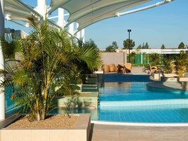 Una piscina con una estructura de sombrilla, rodeada de palmeras y mobiliario de exterior.