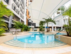 Ein überdachter Pool mit geschwungener Form, umgeben von Palmen und moderner Architektur.