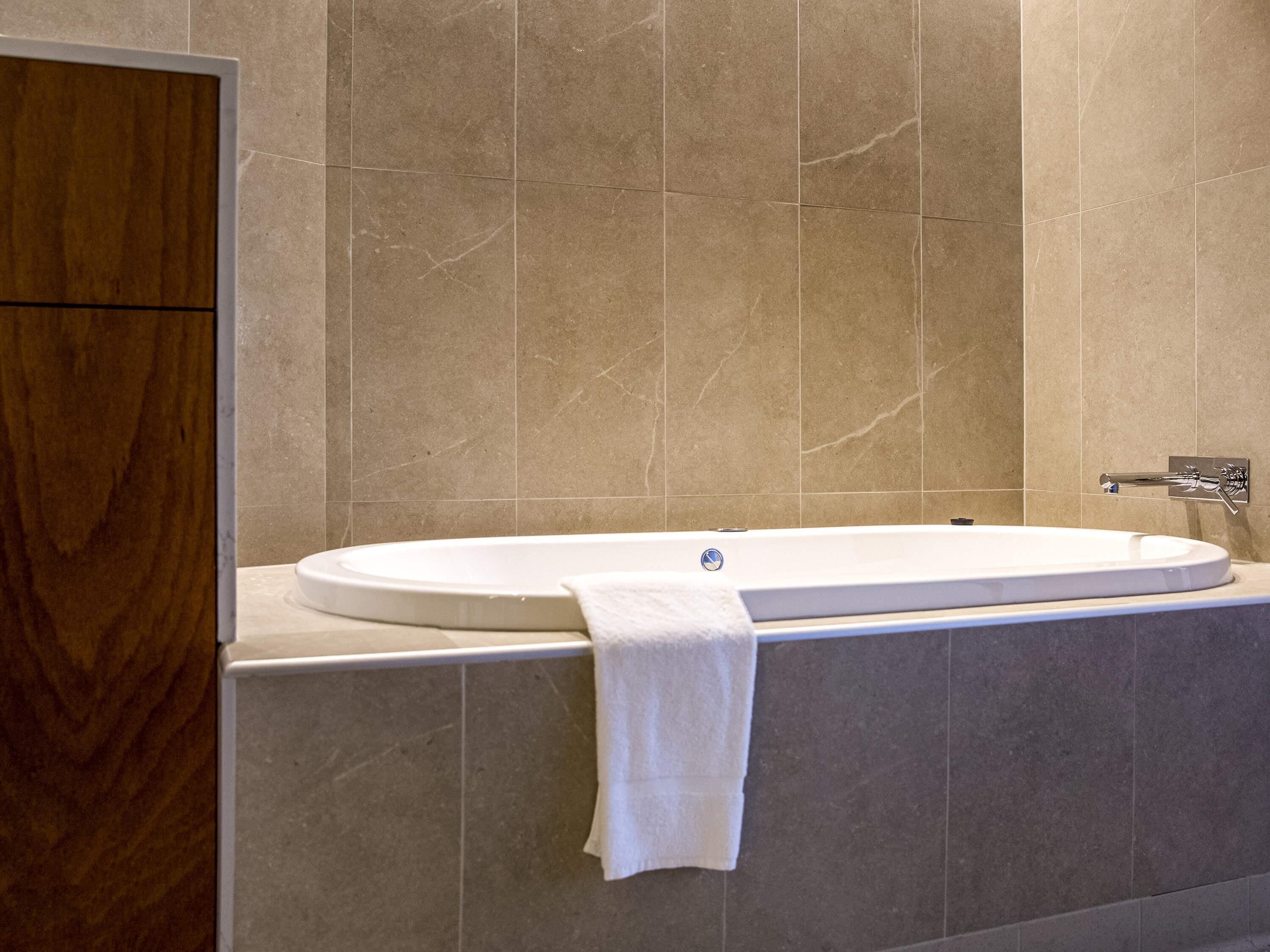 Un baño moderno con una bañera independiente, un mueble de tocador de madera y un muro cubierto de azulejos de mármol.