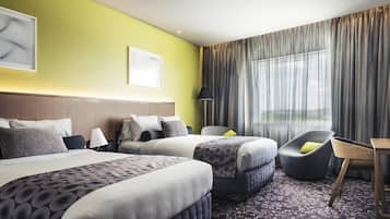 A hotel room with two beds, a desk, a chair, and a large window with curtains.