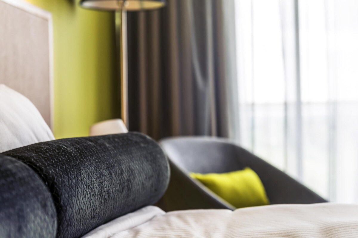 A hotel room with a bed, a chair, a lamp, and a view through the window.