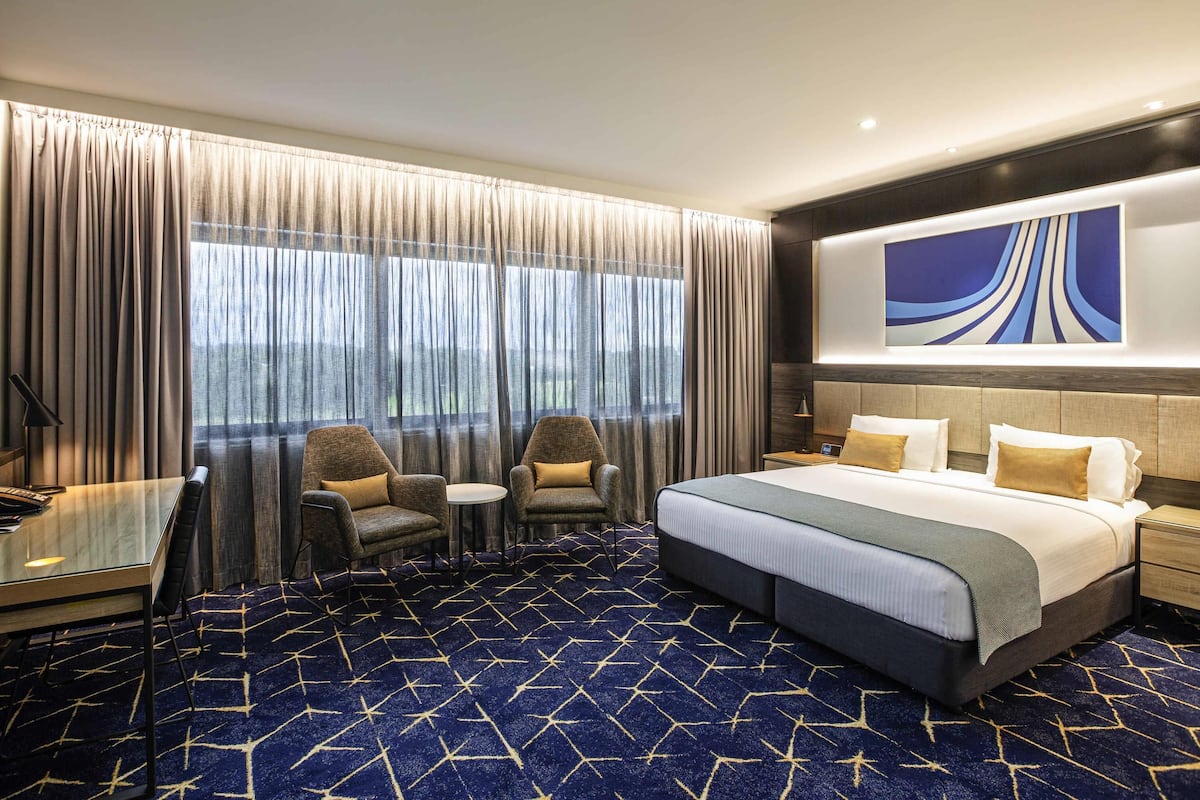 A hotel room with a large bed, two armchairs, a small table, and a desk.