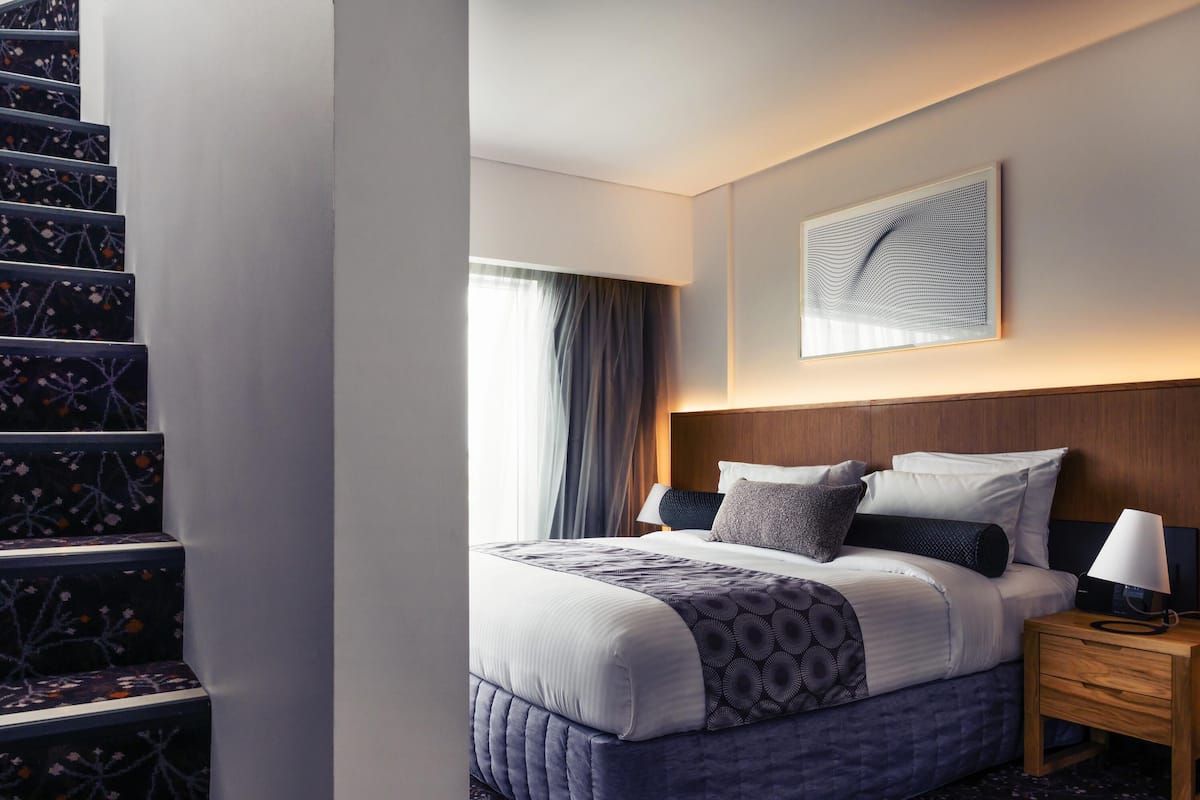 A hotel room with a bed, a nightstand, a wall-mounted artwork, and a staircase with floral-patterned steps.