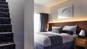Habitación de hotel con cama, mesita de noche, una obra de arte en la pared y una escalera con escalones de estampado floral.