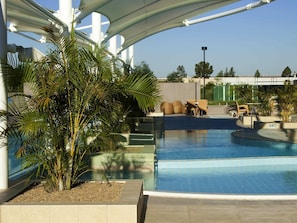 Ein Schwimmbecken mit Palmen, einem überdachten Bereich und Gartenmöbeln.