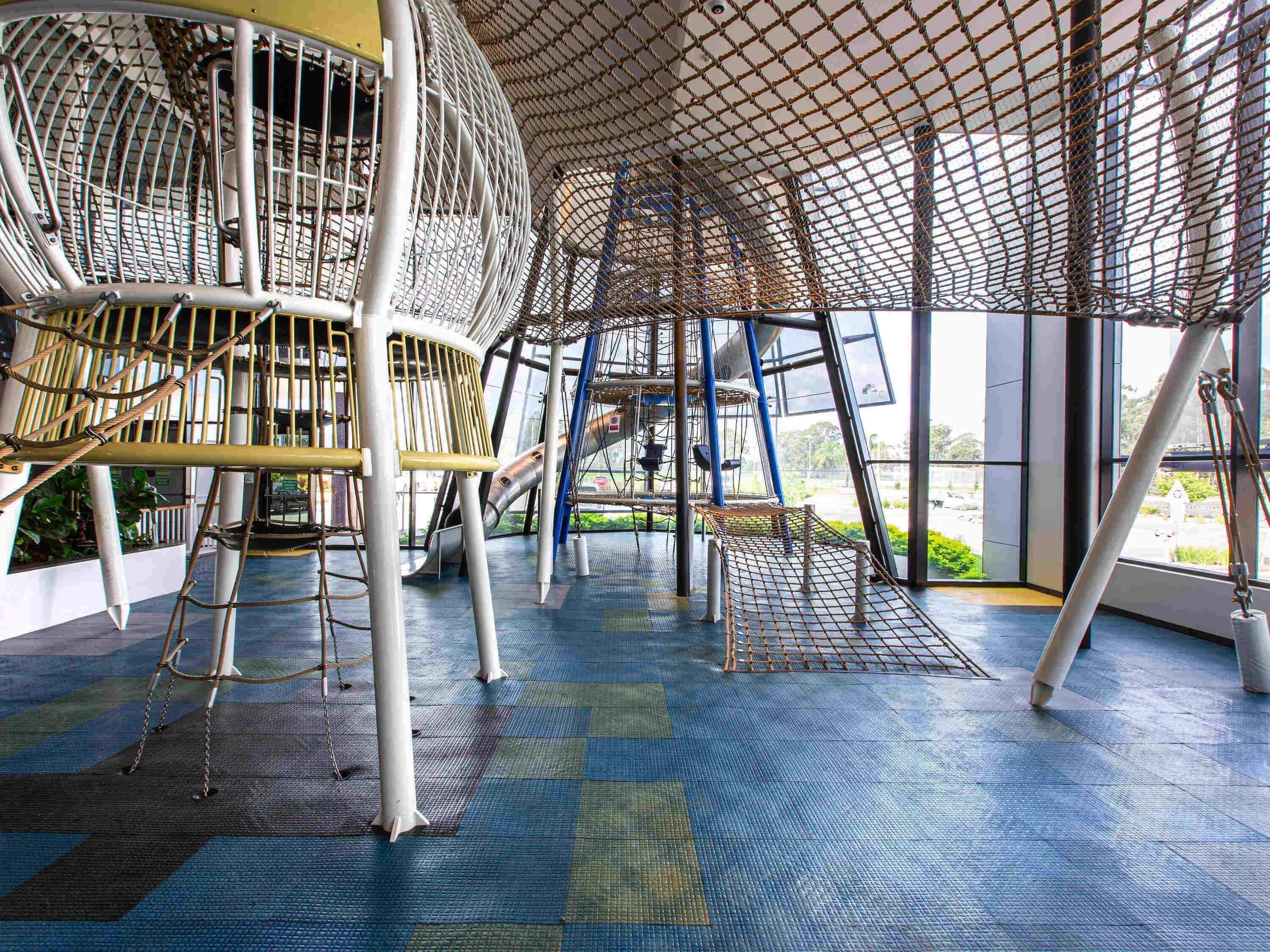 A playground with climbing structures, a slide, and a netted play area.