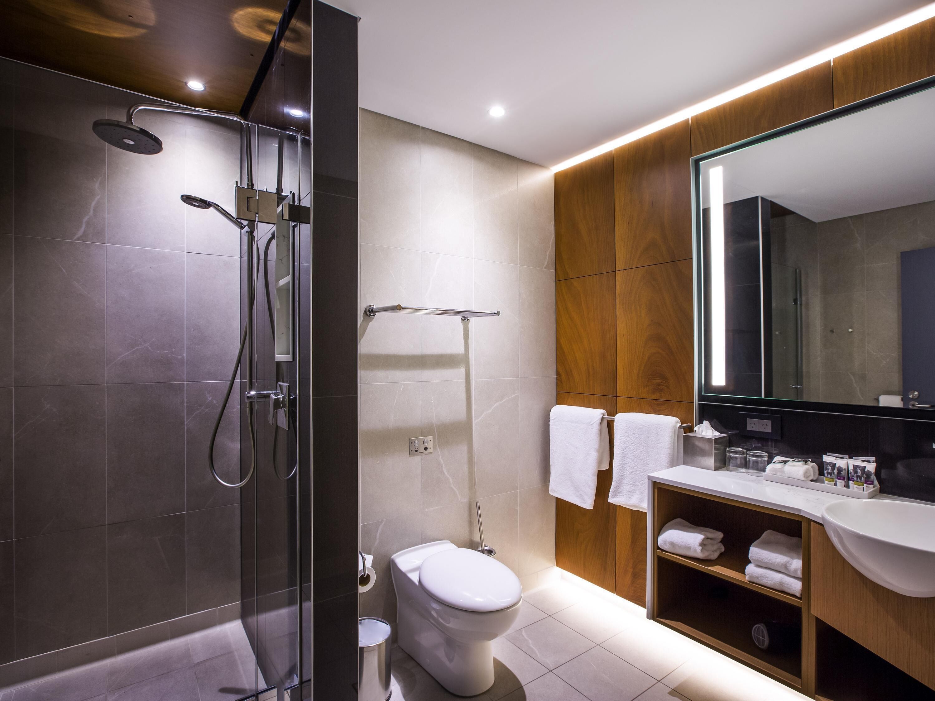 Un baño moderno con ducha de vidrio, inodoro, tocador con espejo y estante con toallas.