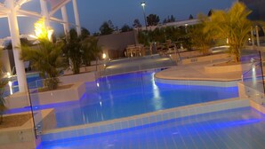 A swimming pool with a blue-lit edge, surrounded by palm trees and outdoor seating. - Mercure Sydney Liverpool (Prestons)
