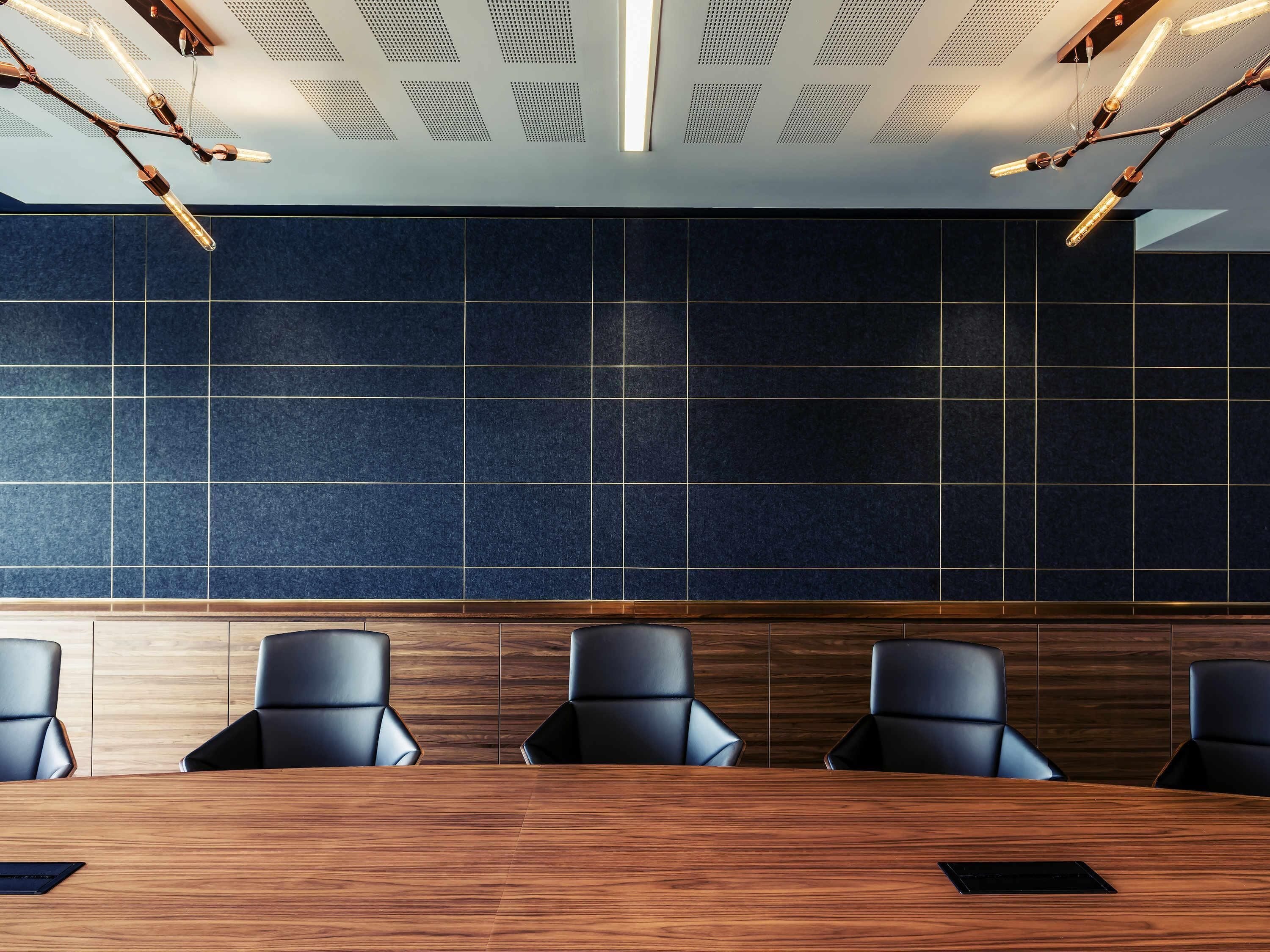 A conference room with a wooden table, black chairs, and a dark tiled wall.