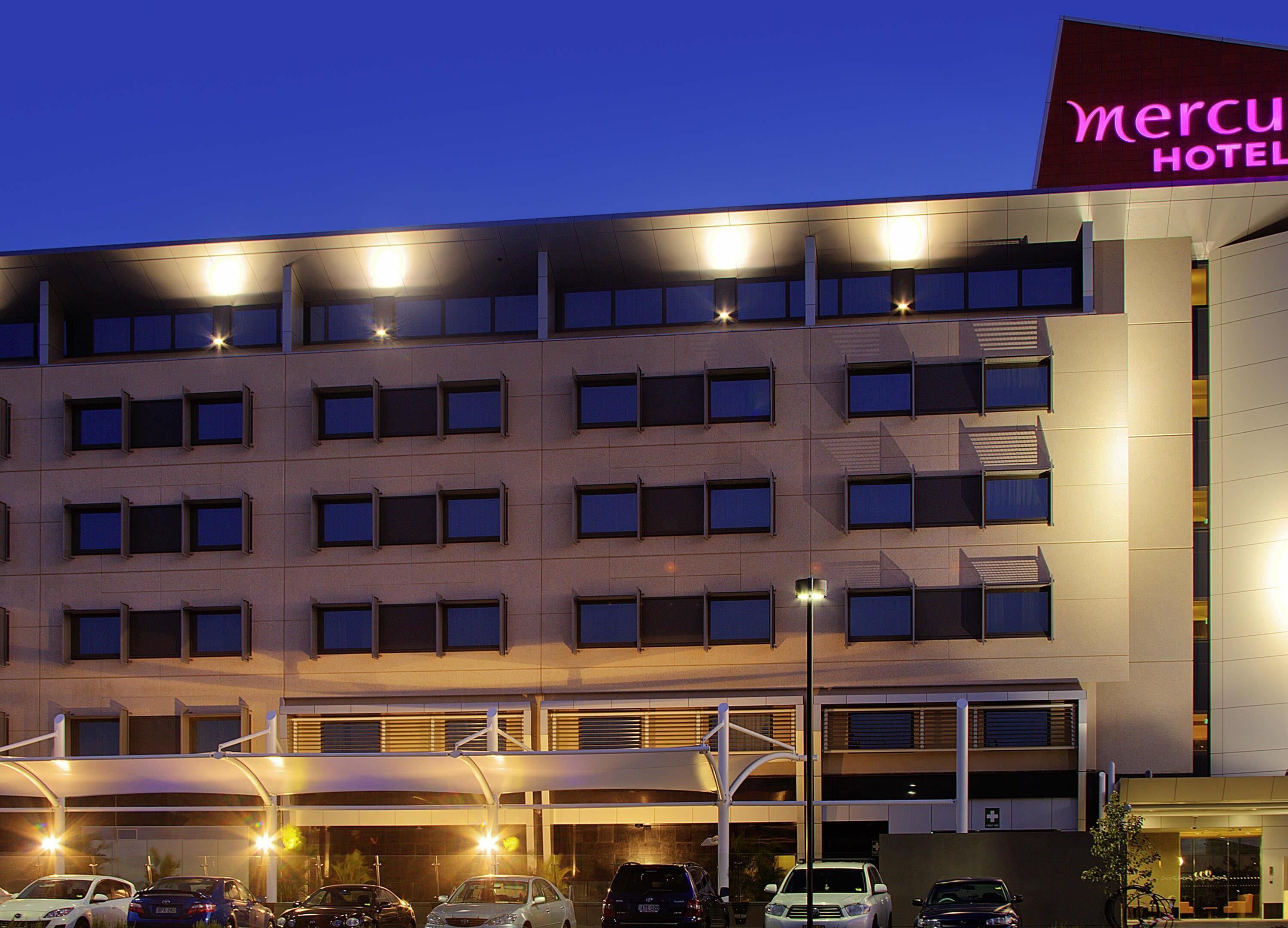 Um edifício moderno de hotel com vários andares, área de estacionamento e entrada visível.