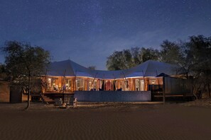 A tented accommodation with a covered outdoor seating area, a fire pit, and a view of the night sky.