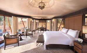 A spacious room with a large bed, a desk, and a chair, with a view of the desert outside.