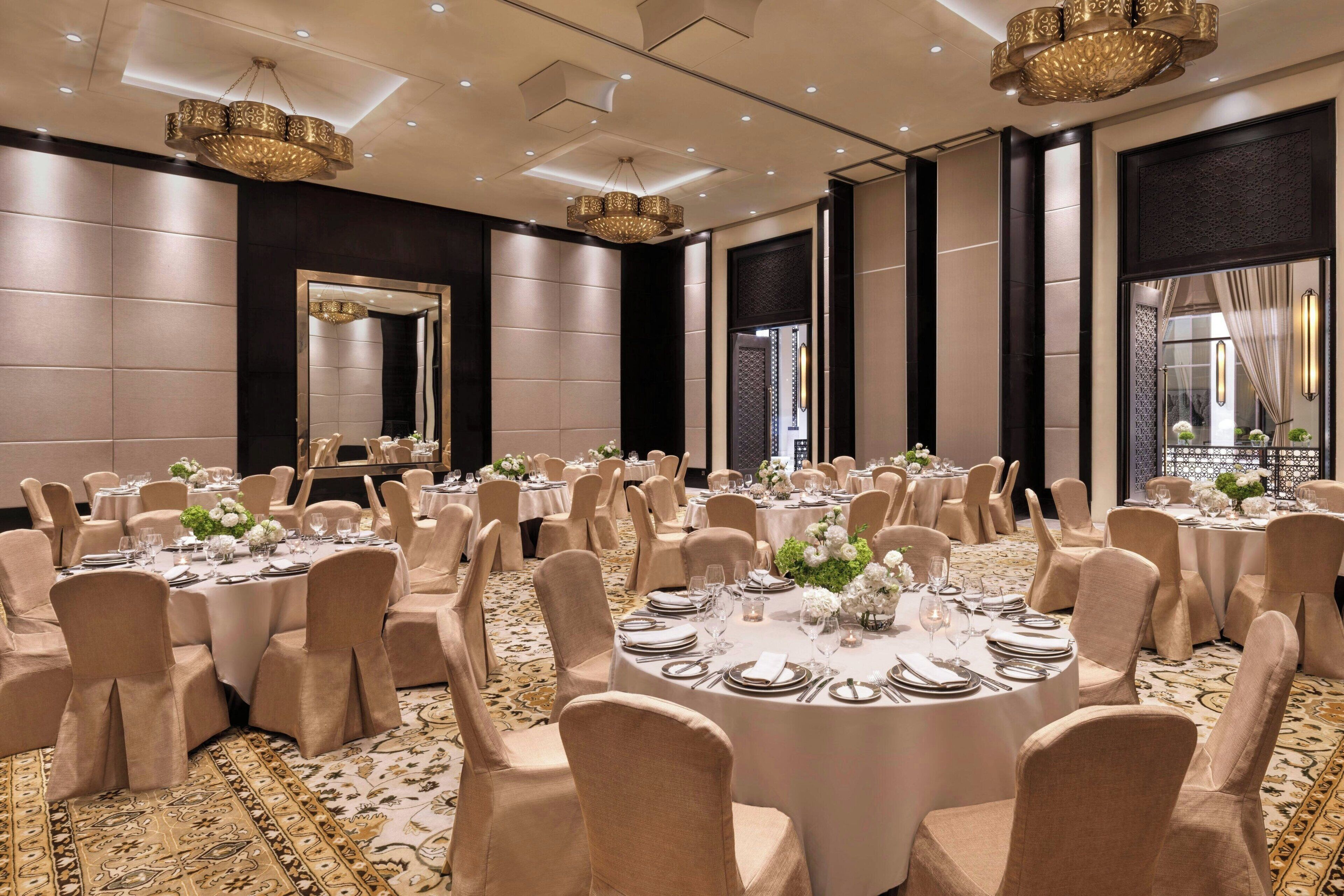 A banquet hall with round tables, beige chairs, and chandeliers.