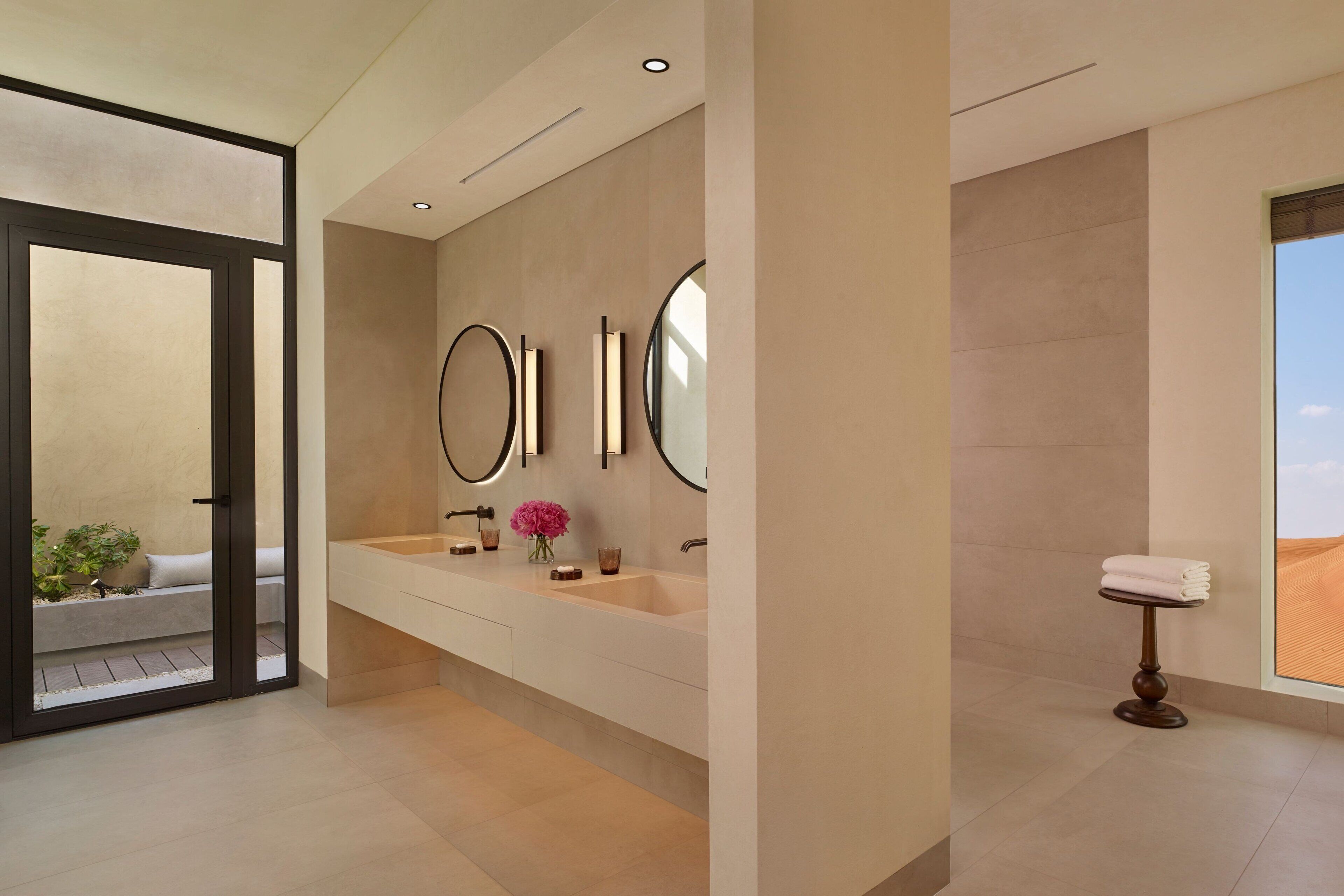 Une salle de bain moderne avec un grand lavabo, deux miroirs et une petite table sur laquelle sont posées des serviettes.