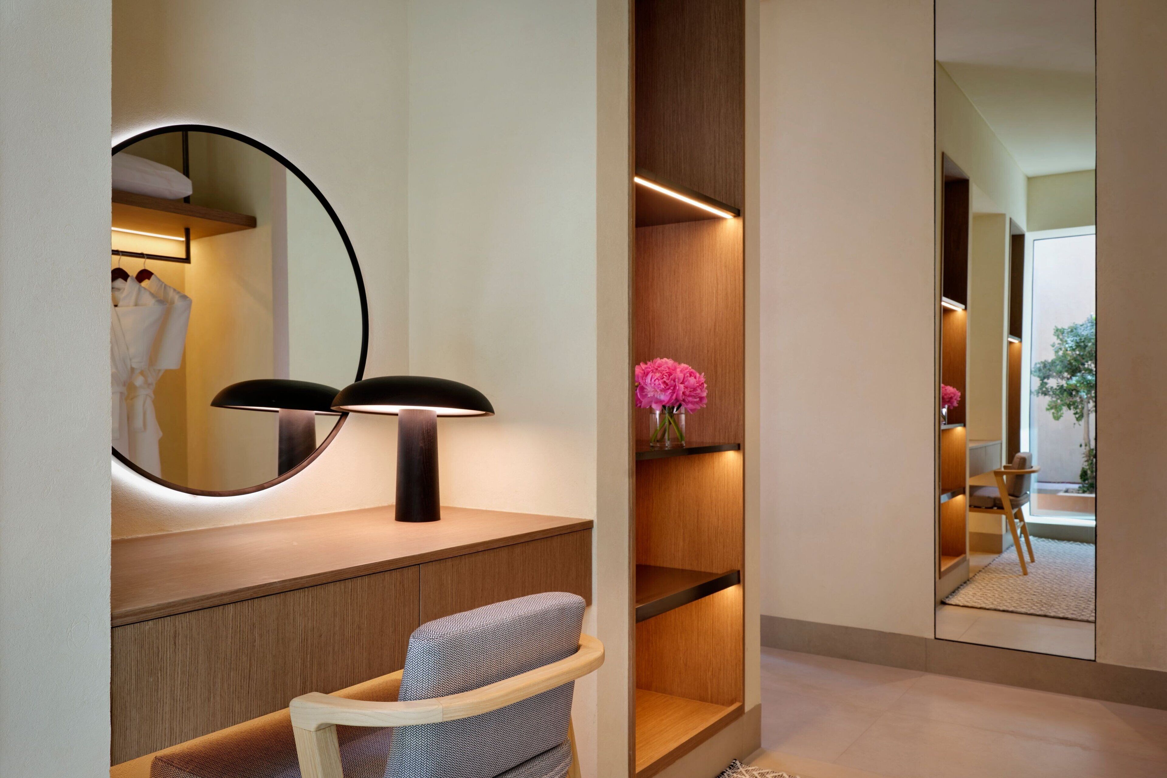 A modern bathroom with a round mirror, a black lamp, a wooden vanity, and a chair.